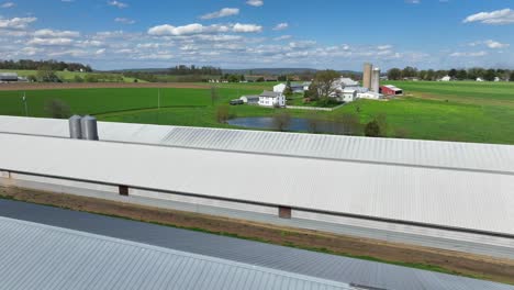 Aerial-orbit-shot-of-stable-barn-on-farm-field-with-house-and-silo-in-background