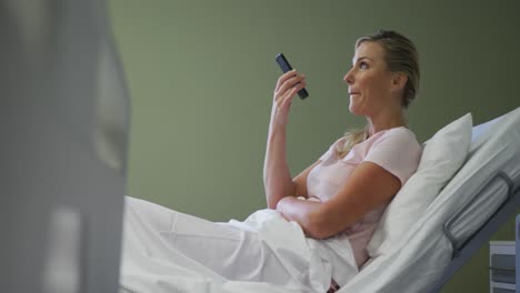 Caucasian-female-patient-lying-in-hospital-bed-talking-on-smartphone