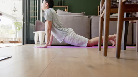 Focused-biracial-man-practicing-yoga-lying-in-living-room,-slow-motion