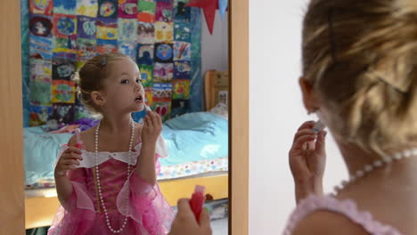a young girl applying lip gloss while playing dress up in the mirror