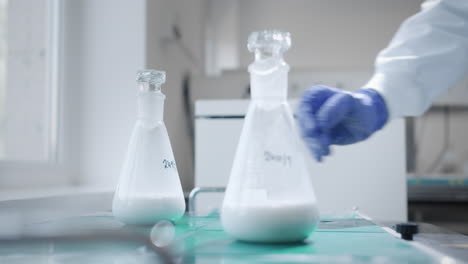 a scientist wearing blue gloves analyzes a white liquid in a conical flask in the laboratory