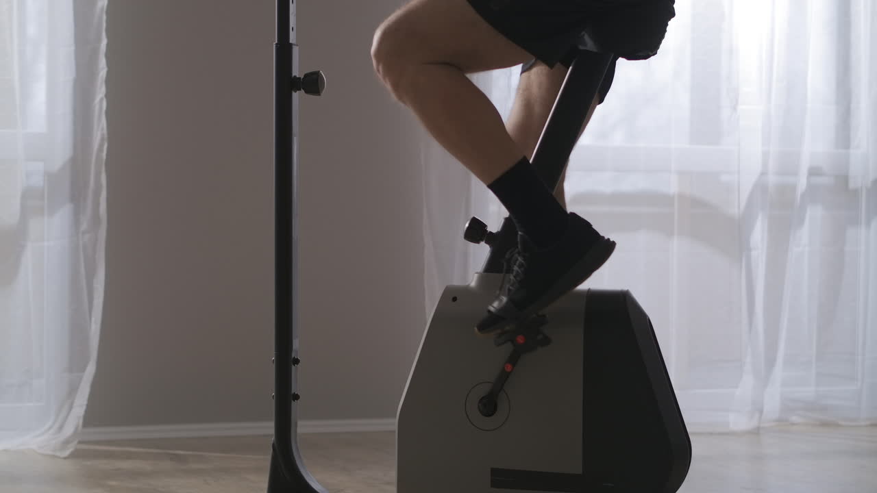 체육관이나 가정에서 스핀링 자전거를 타고 운동하는 중년 남성의 운동은 큰 창문과 함께 벽에 맞춰 노년기에 건강한 생활 방식입니다.