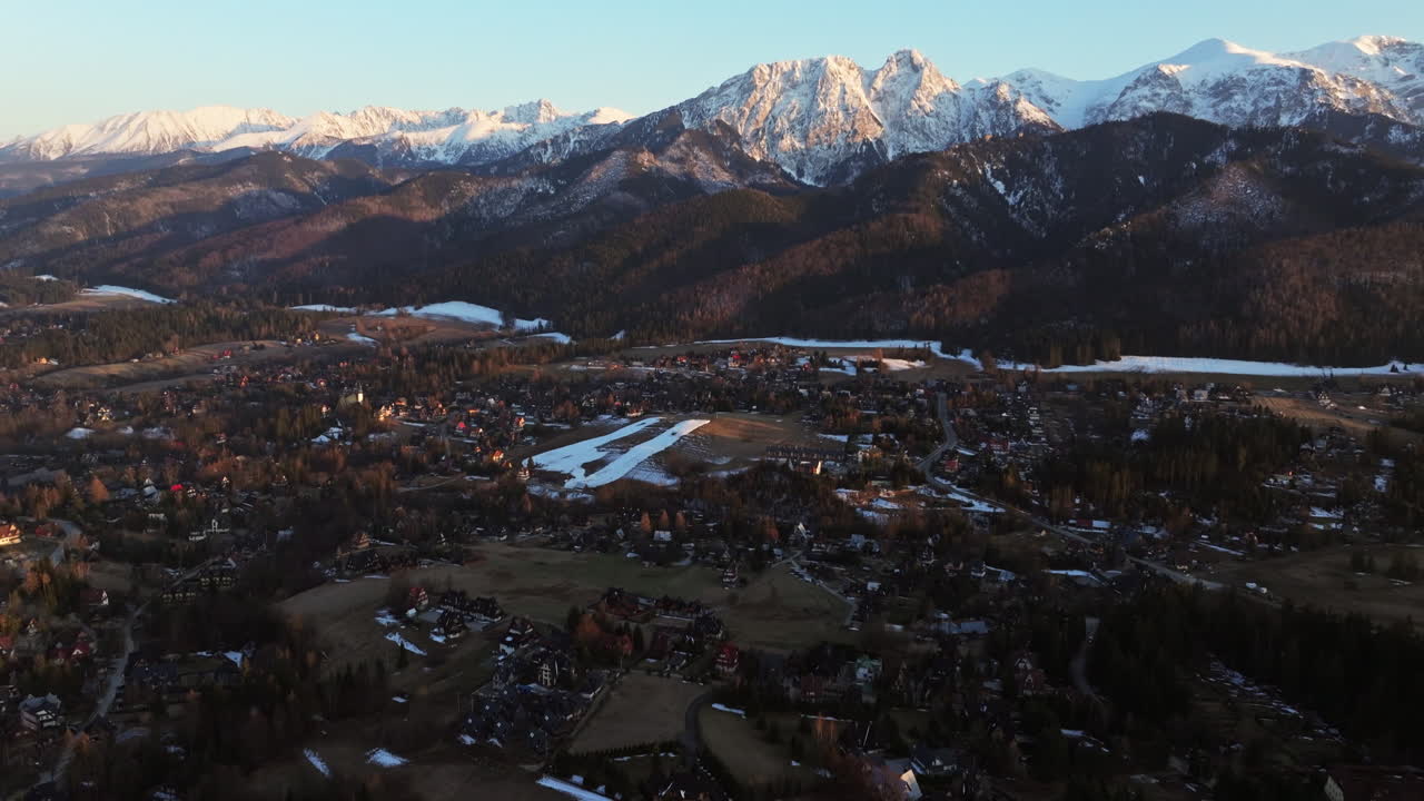 Aerial: Tatra Mountains with snow and Zakopane cityscape at sunrise in Podhale region, Poland, reveal drone shot