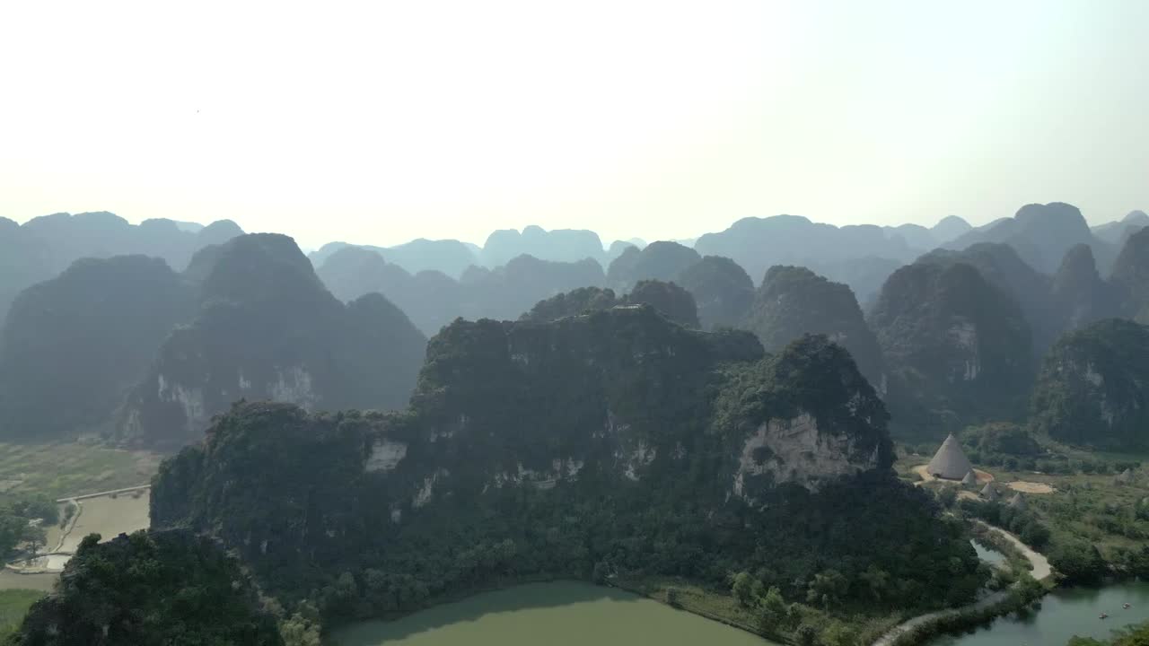 Aerial footage showcasing misty limestone mountains, a quiet lake, and snaking river road in a peaceful natural landscape perfect for cinematic or travel scenes.