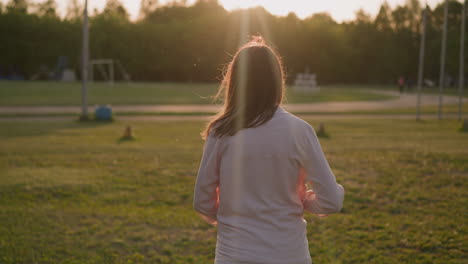 woman wraps long pink shirt walking along ground at sunset