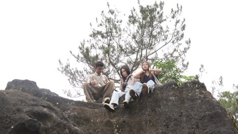 Young Asian Indonesian Friends Chatting and Laughing on Rocky Hilltop in Nature