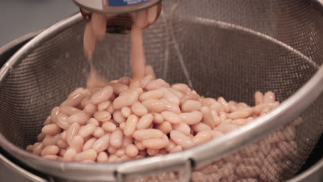 pouring canned white beans into metal mesh colander strainer basket