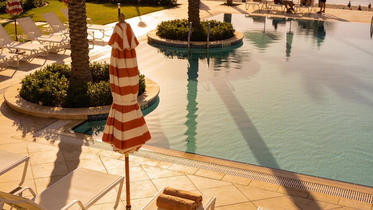 Panning showing red-white umbrella staying closed on resort deck, two people in swimwear strolling