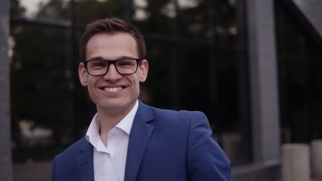 Upwards-footage-of-a-young-businessman-in-elegant-blue-suit-and-glasses-standing-outdoors.-Handsome-businessman-with-his