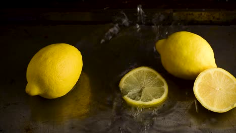grupo de limones enteros con rodajas caídas desde arriba y salpicadas de agua en un ambiente oscuro