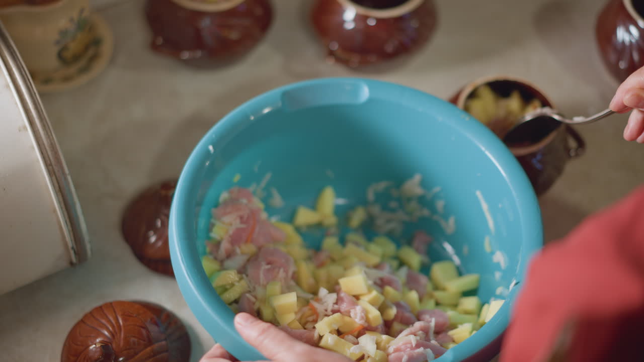 Servizio di insalata di patate e prosciutto. Un cuoco casalingo dimostra vividamente una tecnica precisa per servire l'insalata. Una scena didattica che mostra il trasferimento attento dell'insalata da una ciotola a un barattolo in un ambiente cucina caldo.