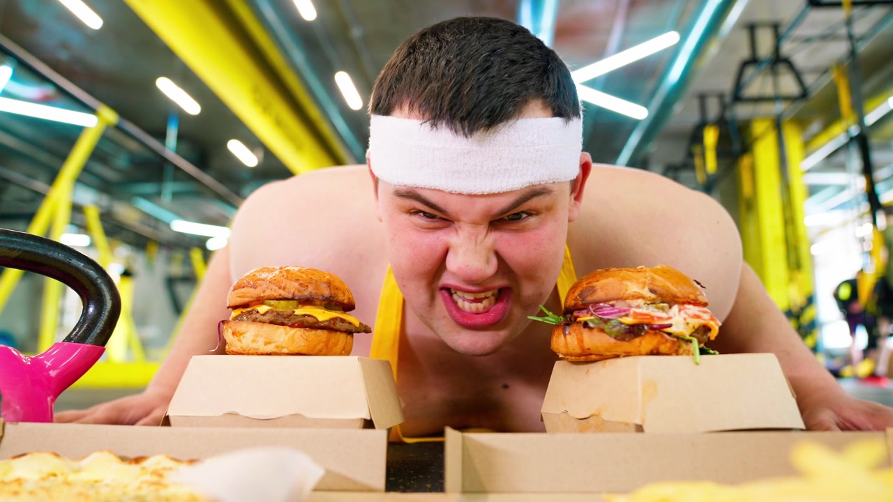 Overvægtig mand kæmper med fastfood-fristelse i et fitnesscenter