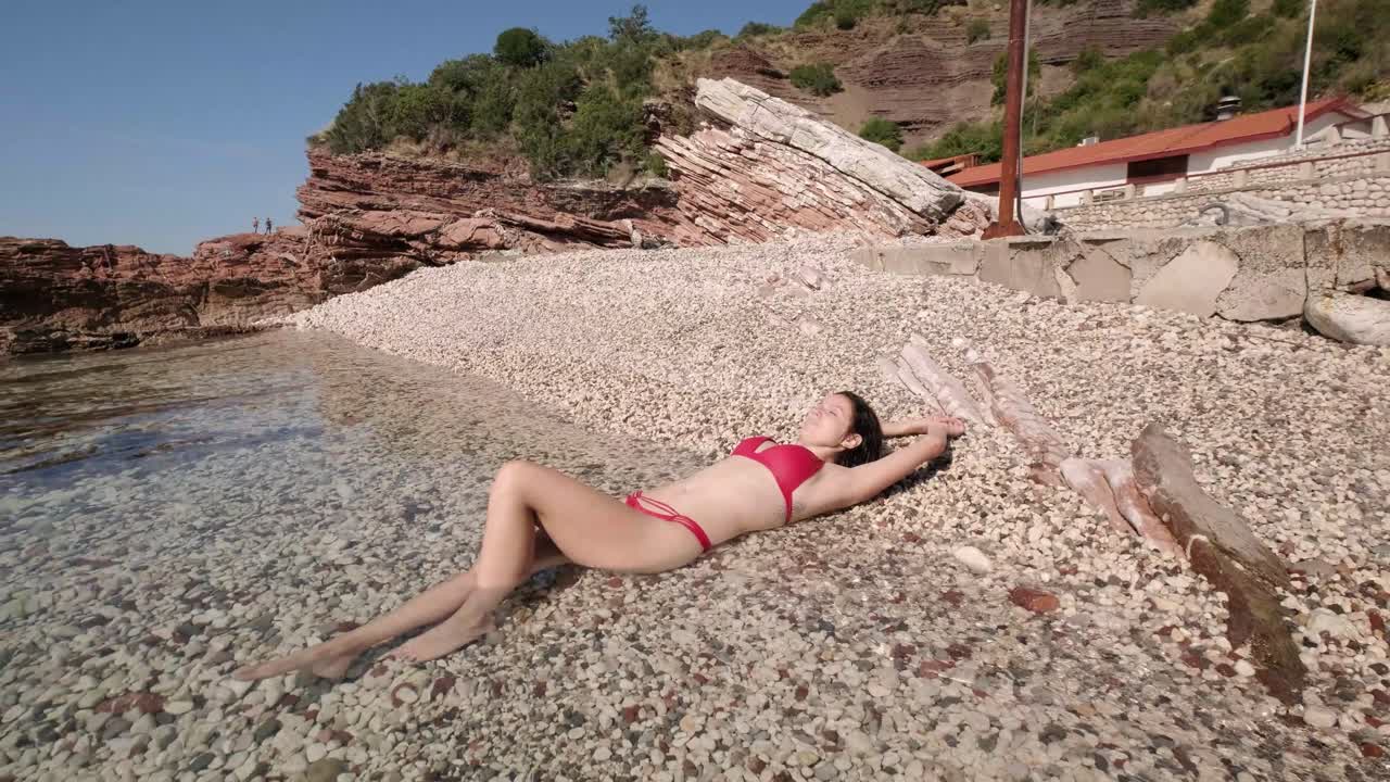 Skinny lady in her red bikinis on the coast of Montenegro on sunny summers days. Small waves crashing on a beautiful body of a girl