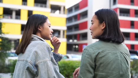 back view of two pretty young japanese girls sitting and talking together outdoors