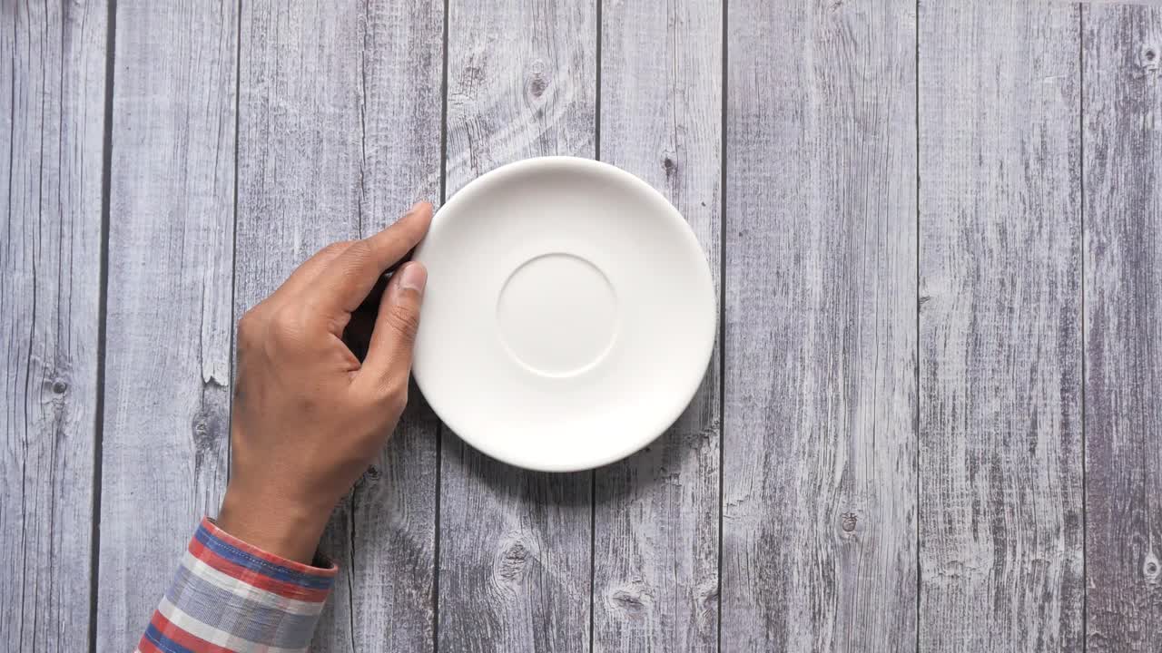 나무 테이블 에 차 컵 과 접시 를 들고 있는 손