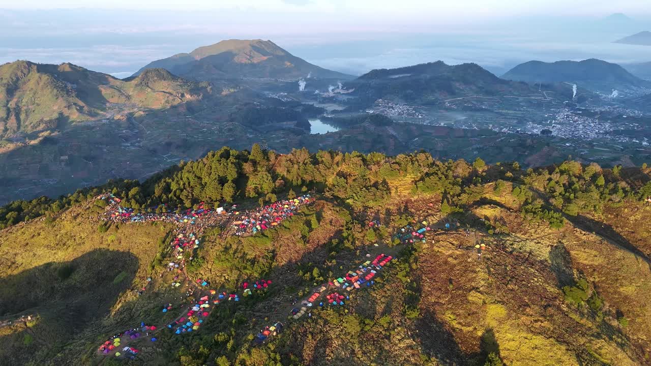 Aerial view of camping spot on grassy muntain ridge with a rich palette of tents and a sweeping view of Indonesia's highland scenery. Scenery of Mount Prau
