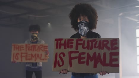 mixed race man and woman wearing face masks holding protest signs