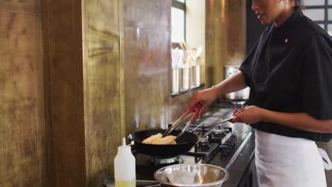 Mixed-race-female-chef-preparing-a-dish-and-smiling-in-a-kitchen-