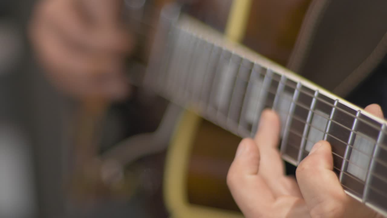 흐릿한 배경이 있는 스튜디오에서 녹음 세션 동안 기타 픽을 사용하여 속이 빈 바디 일렉트릭 기타에서 솔로를 연주하는 전문 음악가를 닫습니다.
