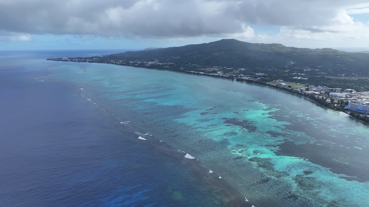 "A stunning aerial drone shot capturing the calm and crystal-clear emerald waters of Saipan’s west coast. Features beautiful coral reefs visible through the transparent sea."