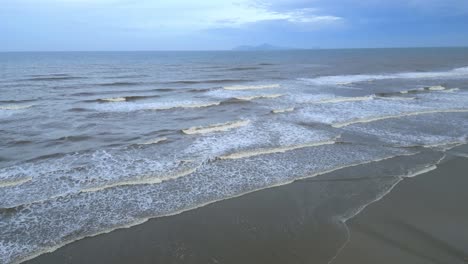 impresionante tiro de inclinación aérea en cámara lenta de las olas blancas del océano golpeando la playa de arena