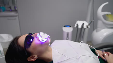 female patient in dental chair in clinic. young woman in protective glasses laying in a dental chair with a special device on her mouth. dentistry concept.