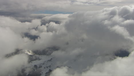toma aérea a través de densas nubes con parches que revelan el paisaje nevado debajo