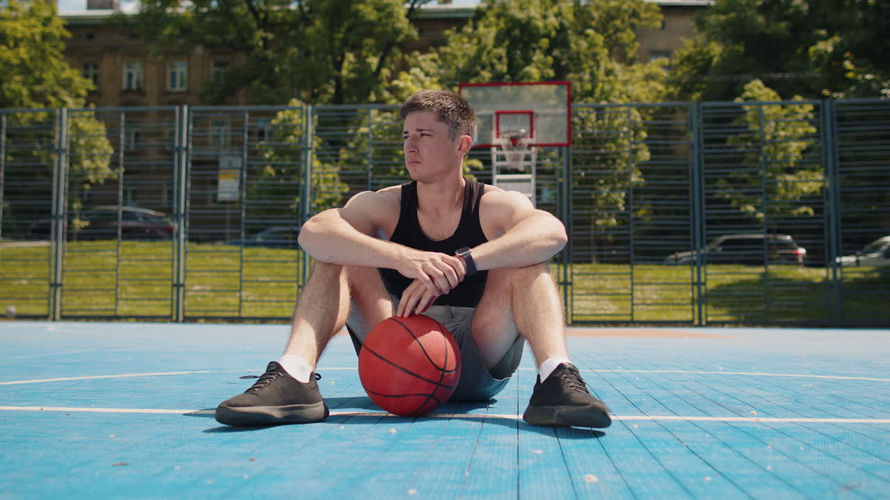 Tired athletic caucasian man in sportswear relaxing after playing basketball game listening music