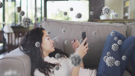 animation of virus cells over biracial woman doing online shopping using smartphone