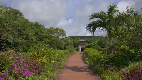 discover the ishigaki cave's entry monument in japan during daylight, encompassed by a vibrant vegetative setting, while the camera steadily moves backward, capturing the essence of this serene site
