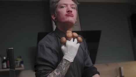 young crazy male chef in an elegant black shirt with an alternative look, tattoos holding mushrooms, spitting one out