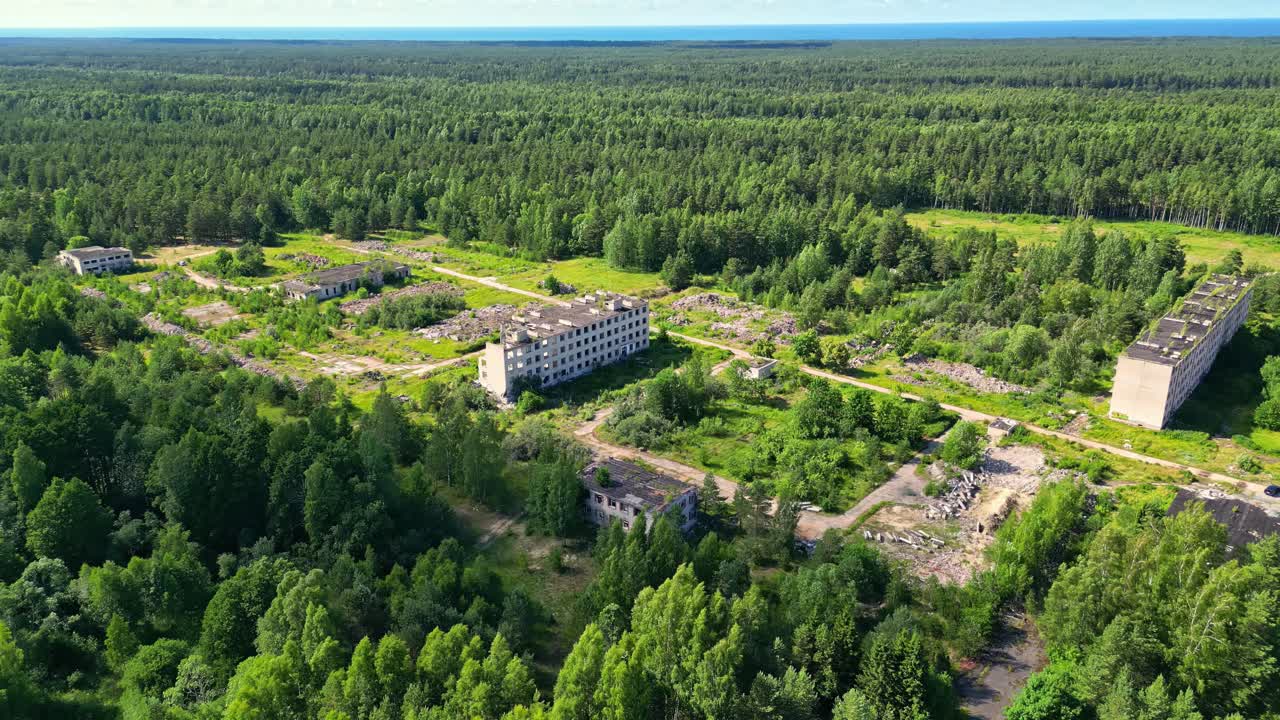 Letecký pohled na hustou lesní krajinu se zříceninami nebo opuštěnými průmyslovými budovami a mýtinami, zachyceno dronem.