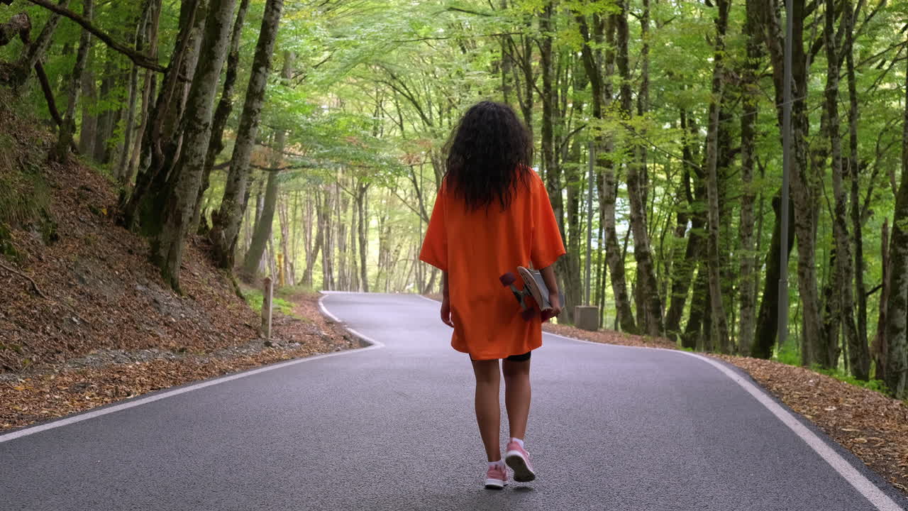 mujer caminando en el bosque con patineta