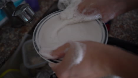 un hombre está lavando un plato blanco en un fregadero lleno de platos sucios