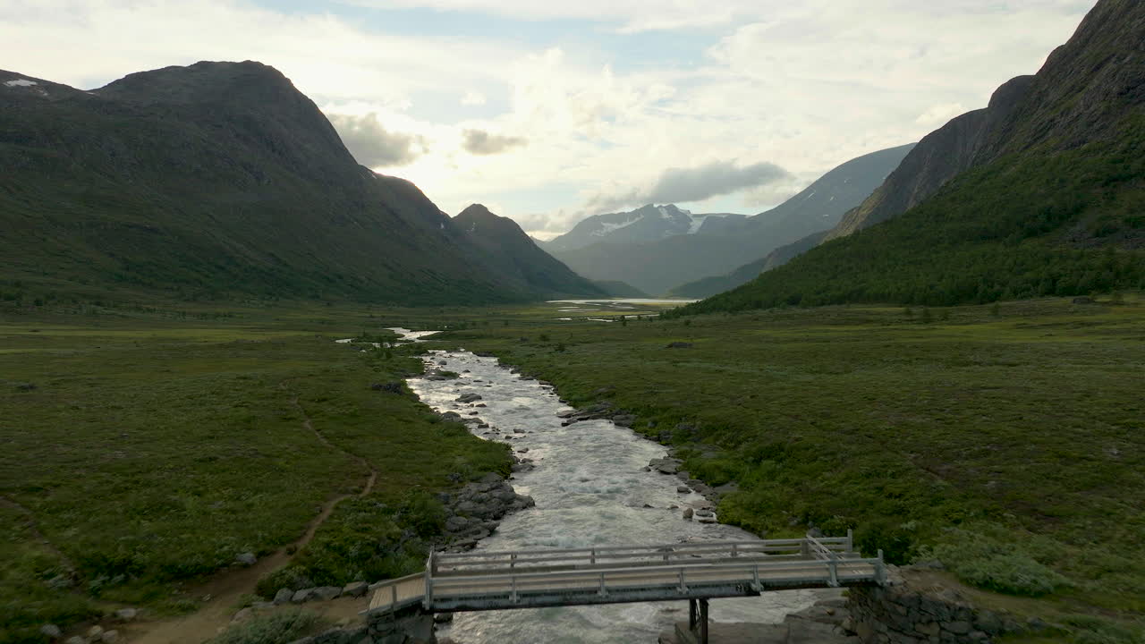 Bugtende flod gennem grønne marker i Jotunheimens bjergrige landskab i Norge.