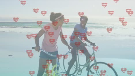 animation of heart icons over happy african american couple cycling at beach