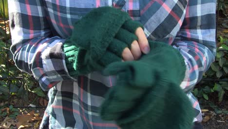 A-young-woman-in-a-park-puts-on-fingerless-gloves-and-rubs-her-hands-together-for-warmth