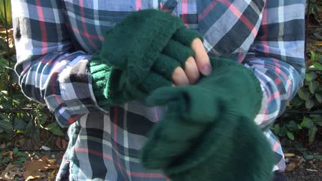 una mujer joven en un parque se pone guantes sin dedos y se frota las manos para calentarse