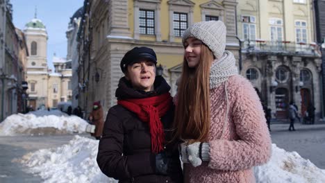 two smiling women sisters tourists walking together on city street, family couple talking, embracing