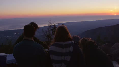 Eine-Gruppe-Von-Freunden-Sitzt-In-Der-Abenddämmerung-Auf-Einem-Campingplatz-An-Der-Küste-Um-Ein-Lagerfeuer