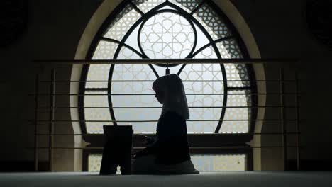Young-hijabi-Muslim-female-reading-Quran-by-window-with-Islamic-style