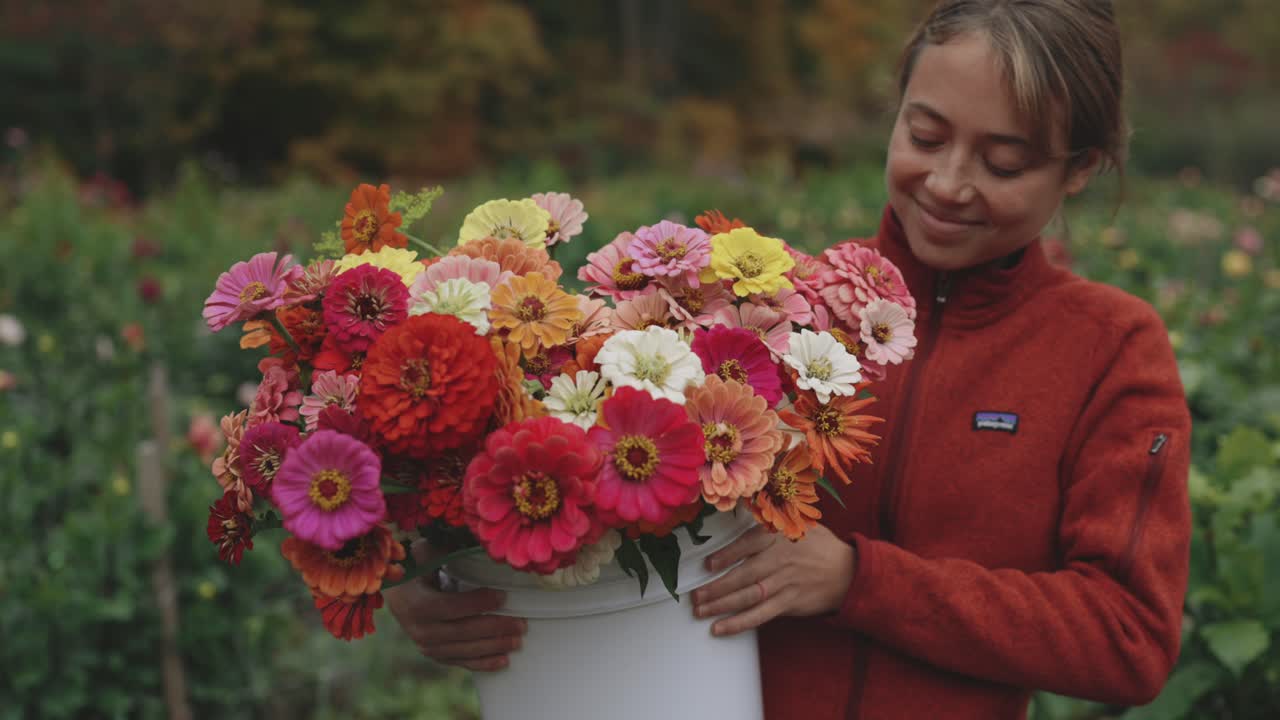 mujer joven sonriente sosteniendo un cubo de flores de zinnia