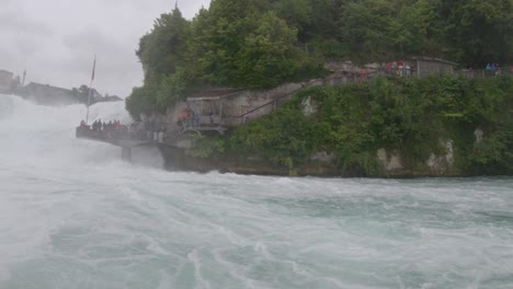 tourists on rhine falls viewing platform as seen during boat ride