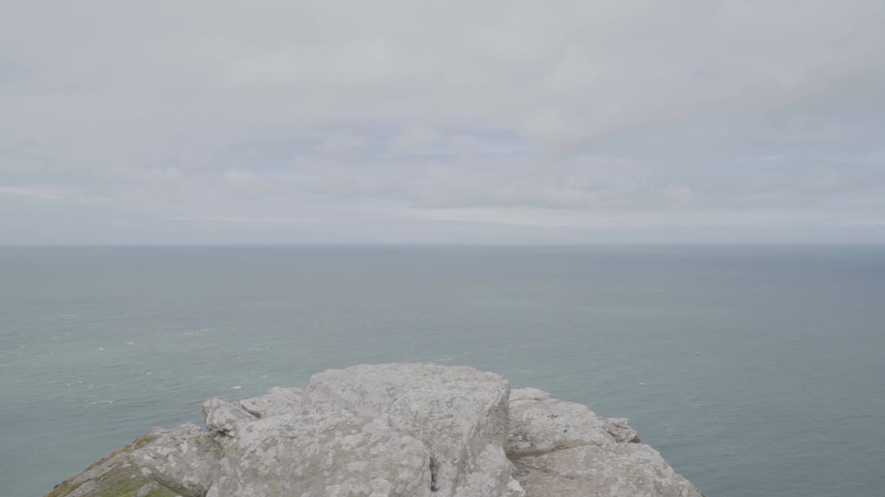 Scogliera costiera che si muove verso il bordo, vista al rallentatore del mare con cielo e nuvole, North Devon, Canale di Bristol, Regno Unito.