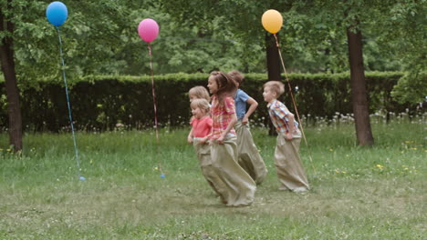 niños jugando a la carrera de sacos en una fiesta de cumpleaños en el parque mientras sus padres los animan