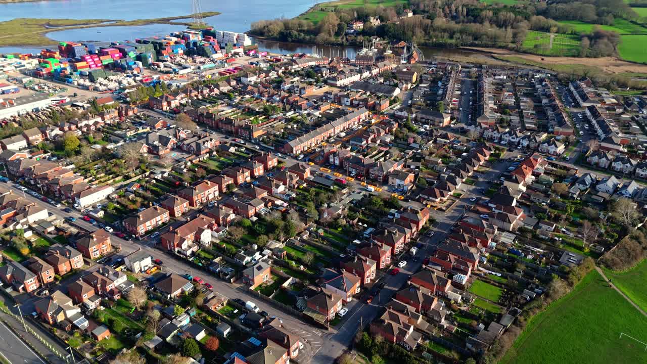 aerial panning shot over the Totton suburb west of the river in Southampton, England with cars driving the busy roads and sunlight reflecting on the blue river water with boats on it in winter
