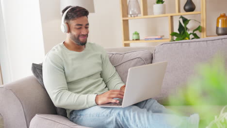 portátil, auriculares y hombre en un sofá en la sala de estar