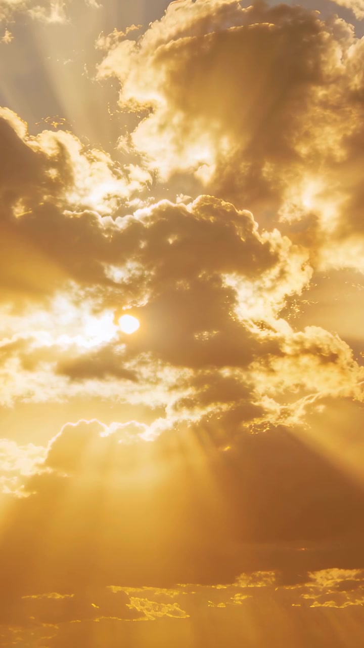 Vertical video: Shifting backlit cumulus casting rays across golden sky while sun partly hiding