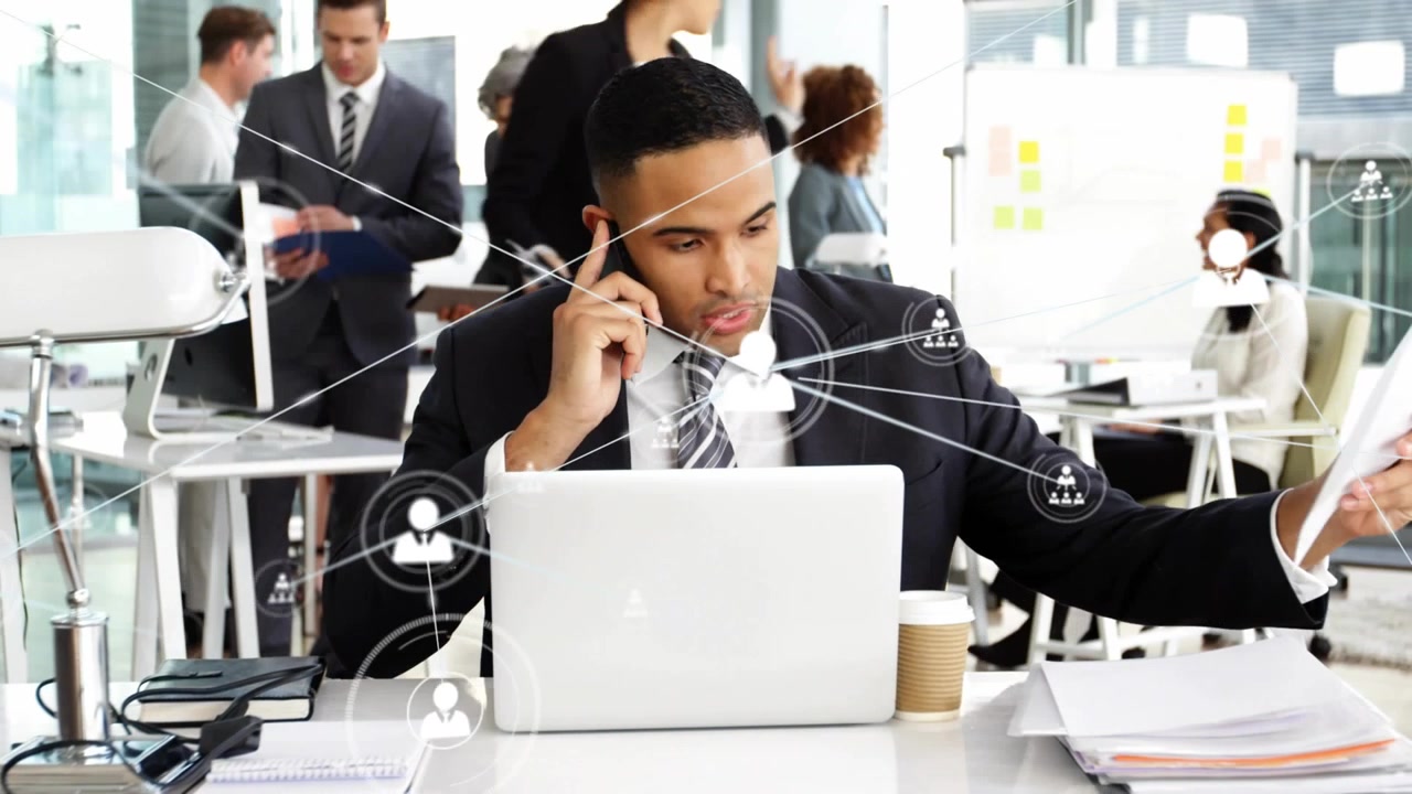 Man houdt telefoon vast, collega geeft documenten aan, sorteert bestanden terwijl een netwerkkaart over de laptop beweegt op kantoor.