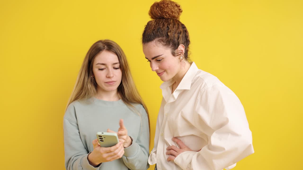 Young women sharing content on smartphone, expressing various emotions on yellow background
